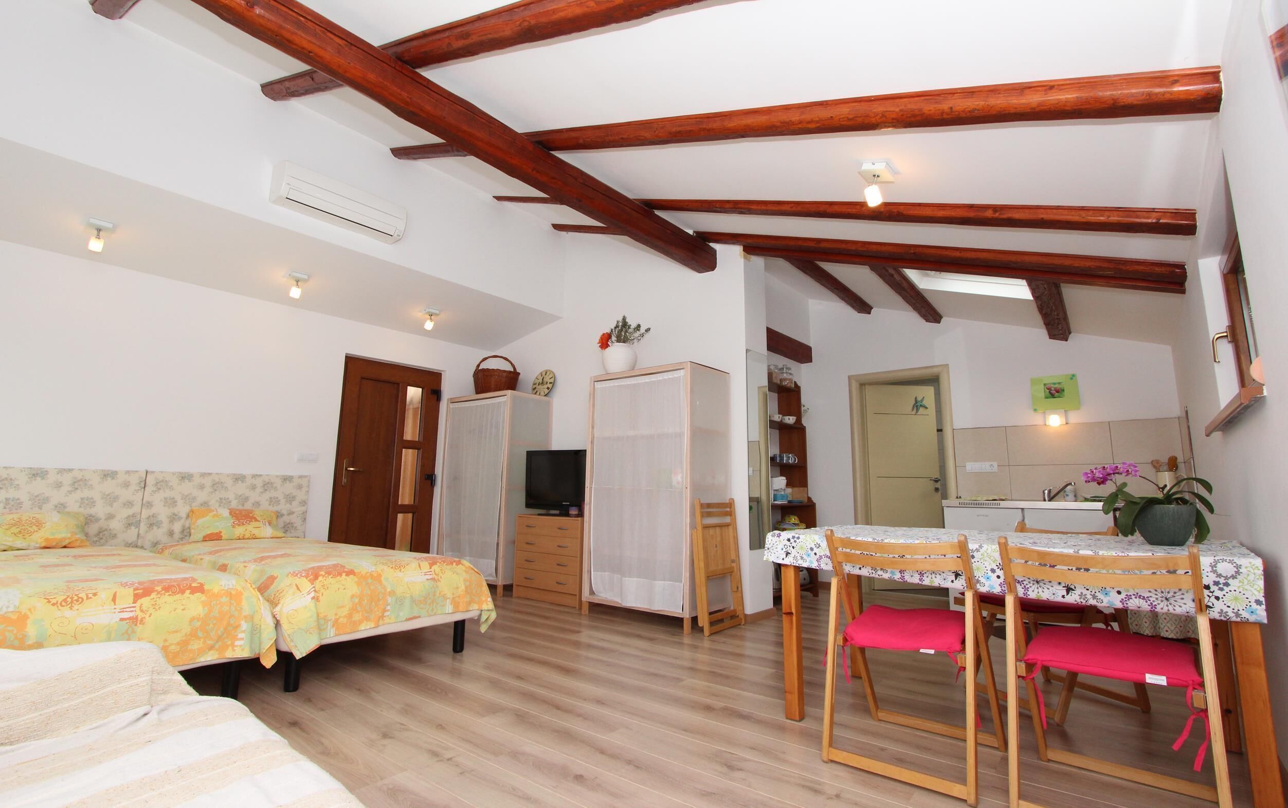 A bedroom with two beds, a wooden ceiling, a TV, a wardrobe, and a small table with chairs.