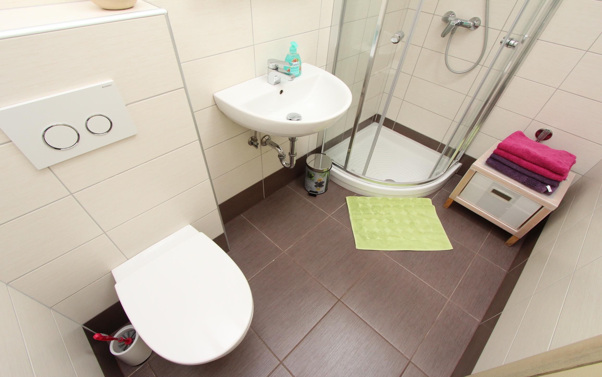 A bathroom with a toilet, sink, shower, and a small storage unit with towels.