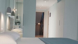 Une chambre d’hôtel moderne avec un lit aux lignes courbes, des luminaires suspendus et un grand miroir.