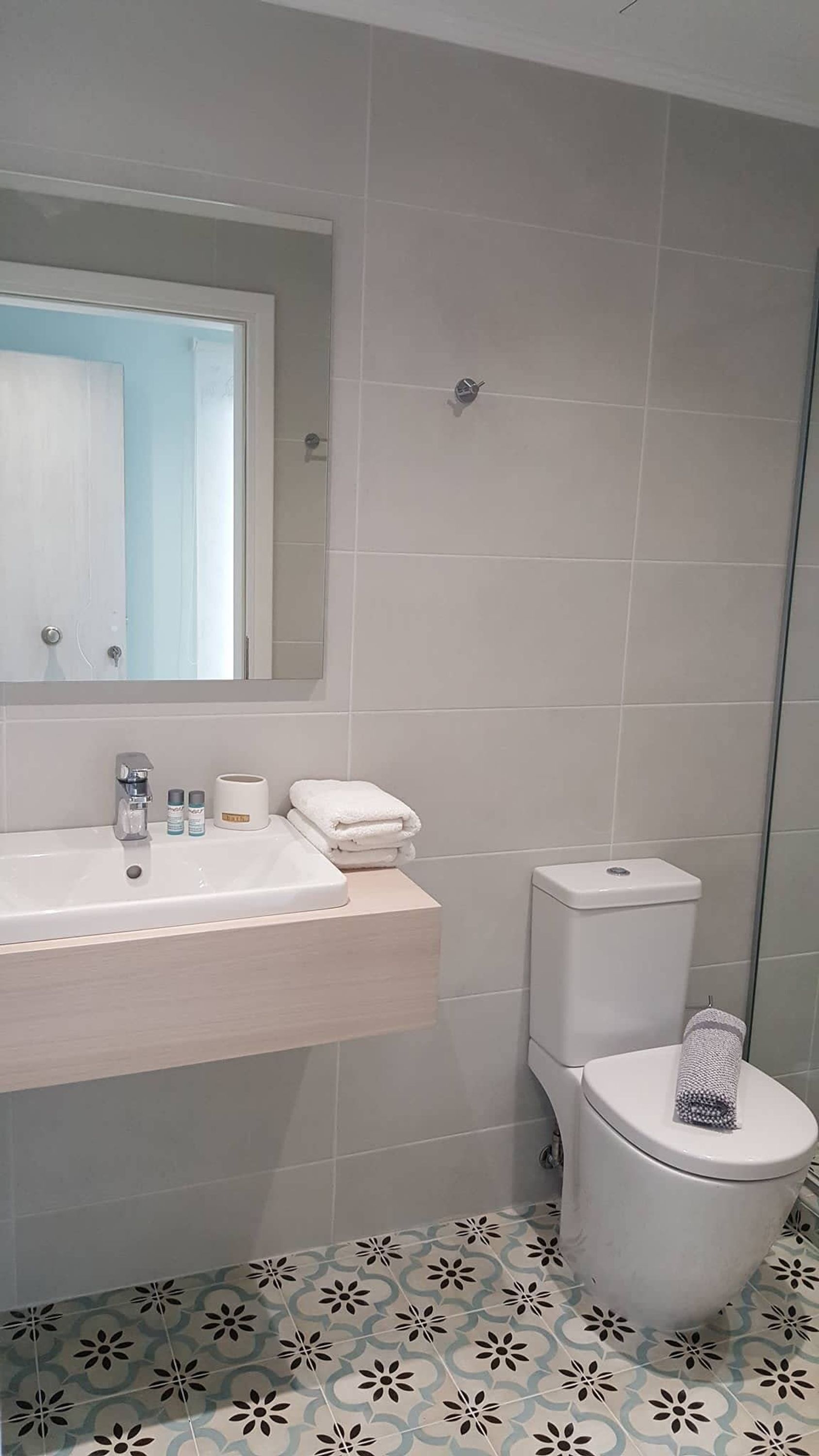 A bathroom with a white sink, mirror, and toilet. There are towels and toiletries on the sink.