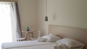 A large bed with white linens, a bedside table, a hanging light, and a window with curtains. - Mear Garden Studio - Cozy Garden Getaway (Kantanos-Selino)