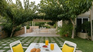 An outdoor patio with a white table set for breakfast, including croissants, coffee, and orange juice. - Mear Garden Studio - Cozy Garden Getaway (Kantanos-Selino)