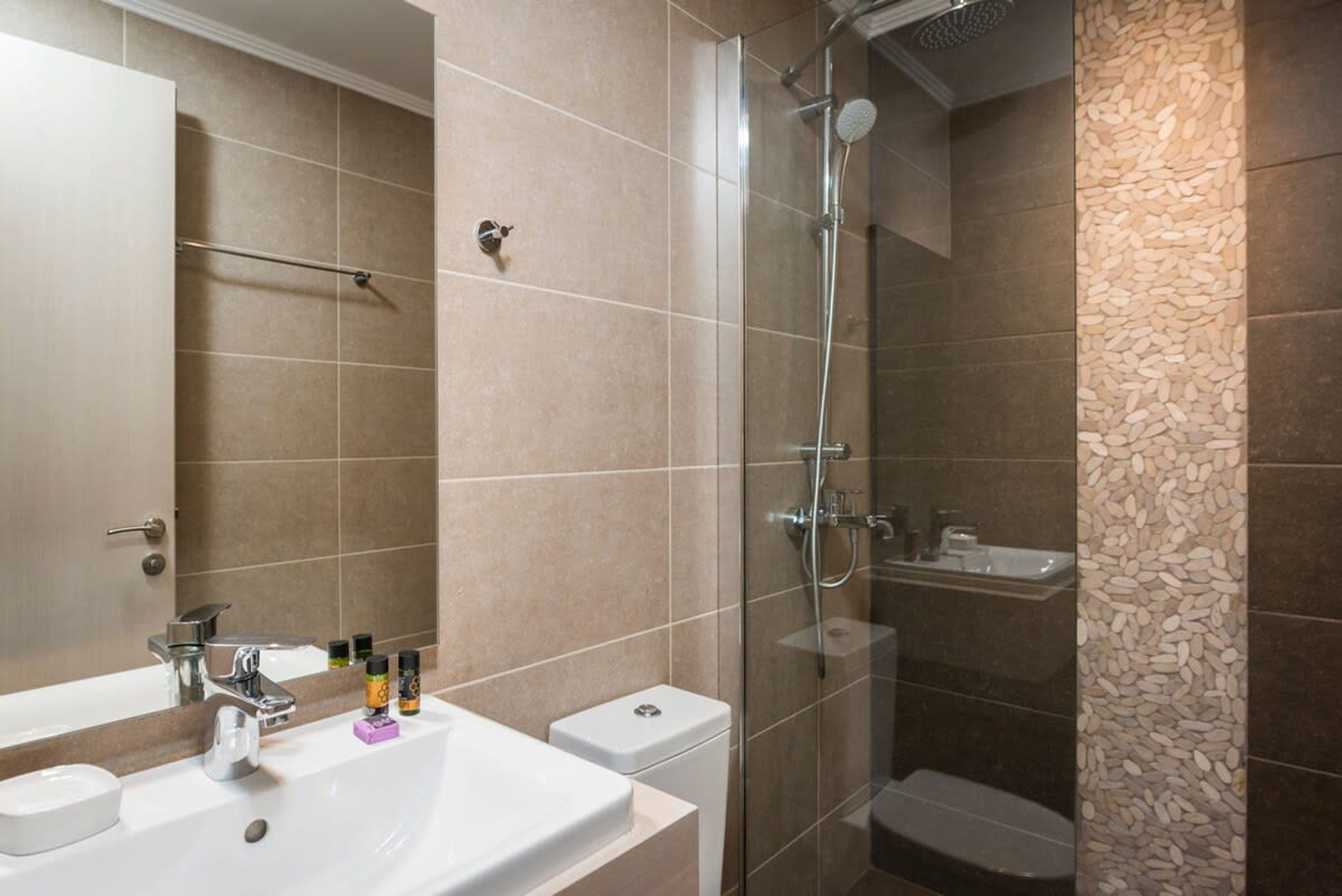 A modern bathroom with a glass-enclosed shower, a white sink with a mirror, and a toilet.