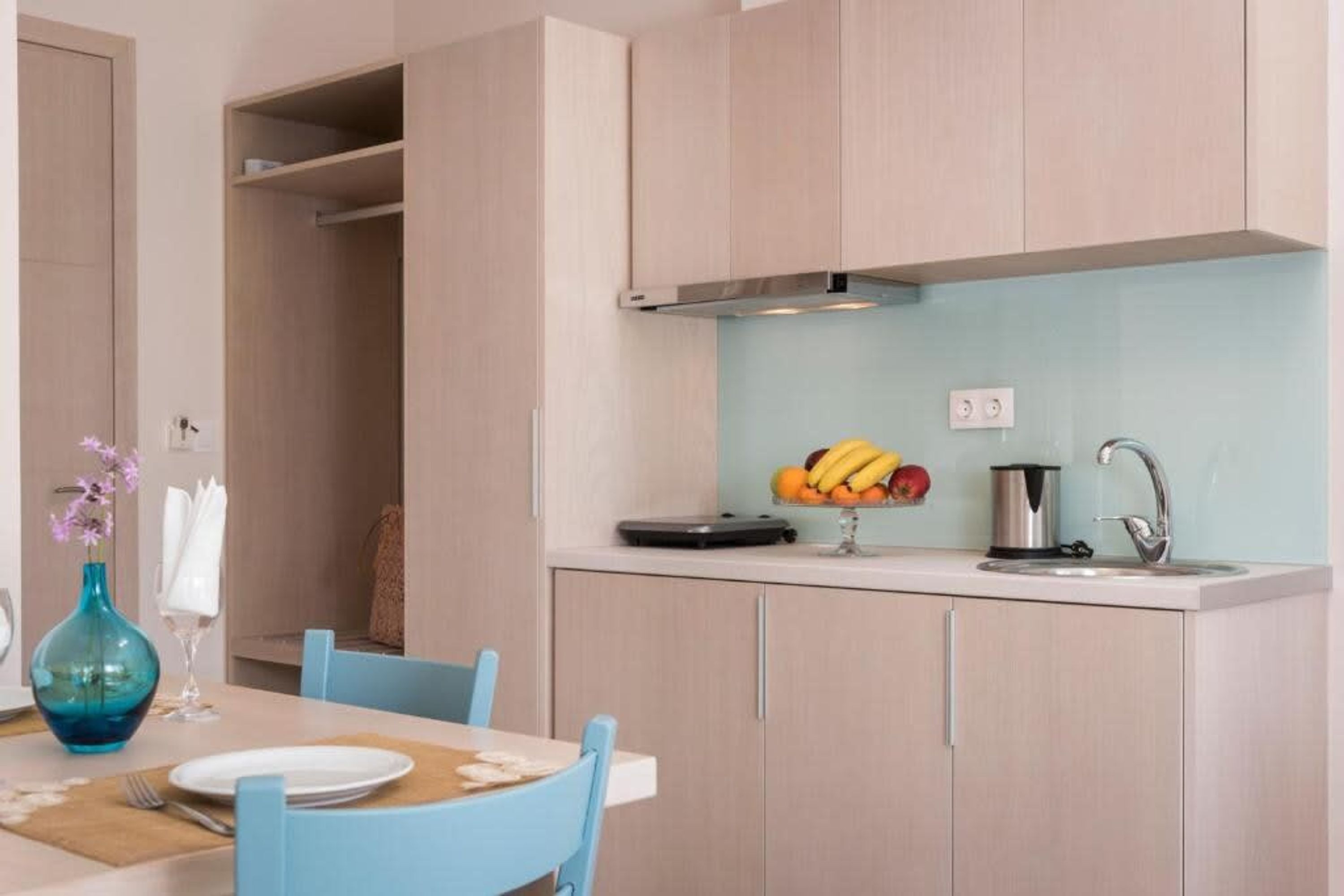 A modern kitchen with light wood cabinets, a white countertop, and a fruit bowl.
