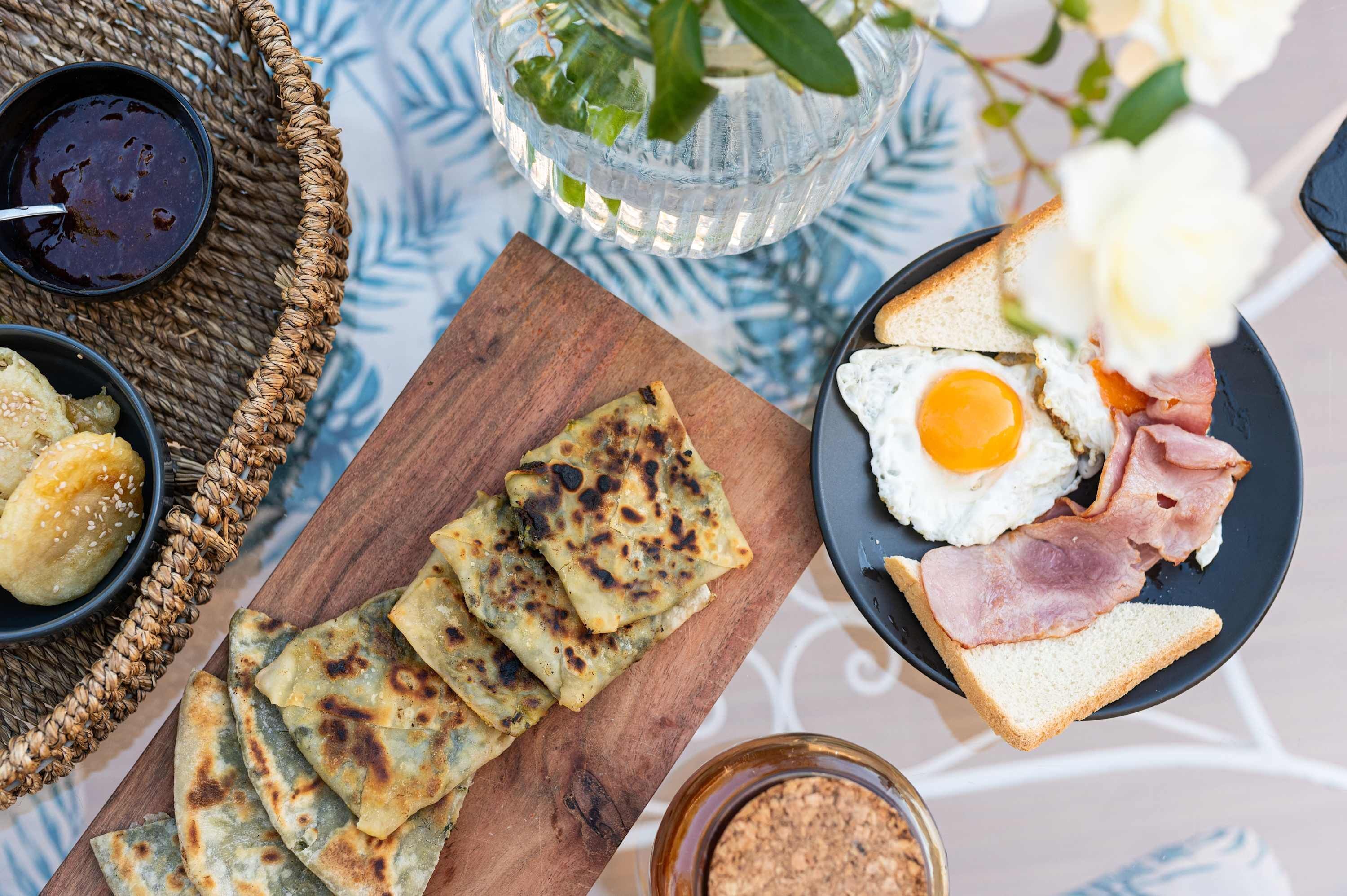 A breakfast setting with toast, eggs, ham, and flatbreads on a wooden board.