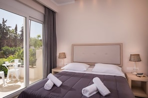 A hotel room with a large bed, two bedside tables with lamps, a sliding glass door to a balcony with outdoor furniture, and a view of greenery outside. - Mear Superior Home - Crete Garden Escape (Kantanos-Selino)