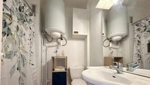 A modern bathroom with a white sink, toilet, and shower. There is a shelf with toiletries and a towel rack.