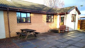 A brick building with a tiled roof, a picnic table, and a bench. - Charming two-bedroom pet friendly property with fire (Aviemore)