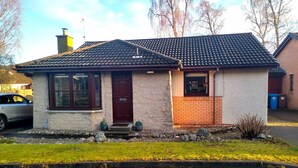 A single-story house with a dark tiled roof, a front door, and a small porch area. - Charming two-bedroom pet friendly property with fire (Aviemore)