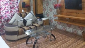 Una sala de estar con un sofá, una mesa de centro de vidrio, un televisor montado en una pared de madera y un equipo de aire acondicionado.