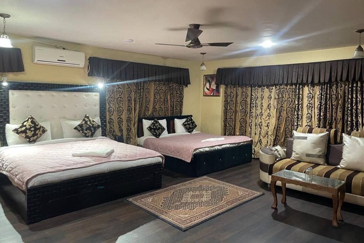 A hotel room with two beds, a sofa, a coffee table, and a ceiling fan.