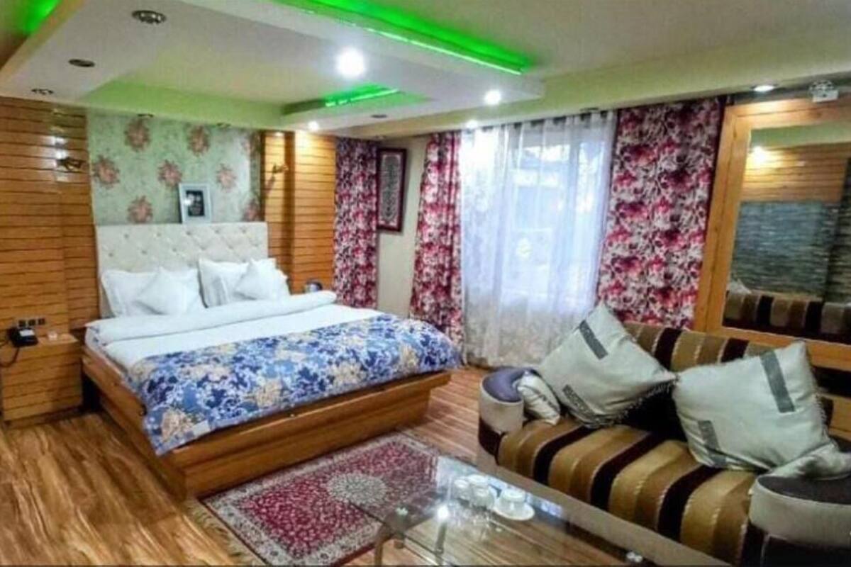 A bedroom with a large bed, a sofa, a glass coffee table, and a wooden floor.