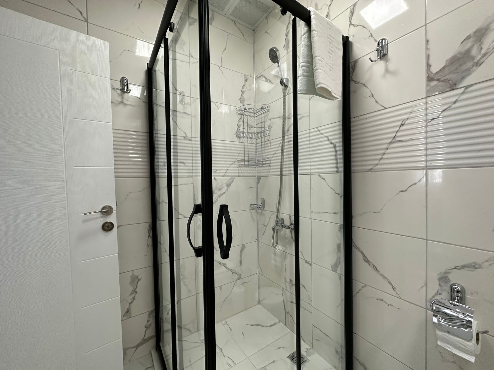 Eine begehbare Dusche mit Glaswänden, einer Wand aus Marmorplatten, einem Handtuchhalter und einer Duschbrause.