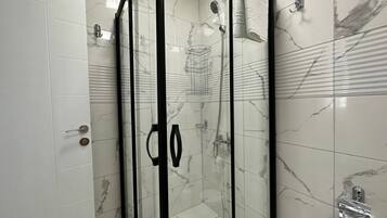 Eine begehbare Dusche mit Glaswänden, einer Wand aus Marmorplatten, einem Handtuchhalter und einer Duschbrause.