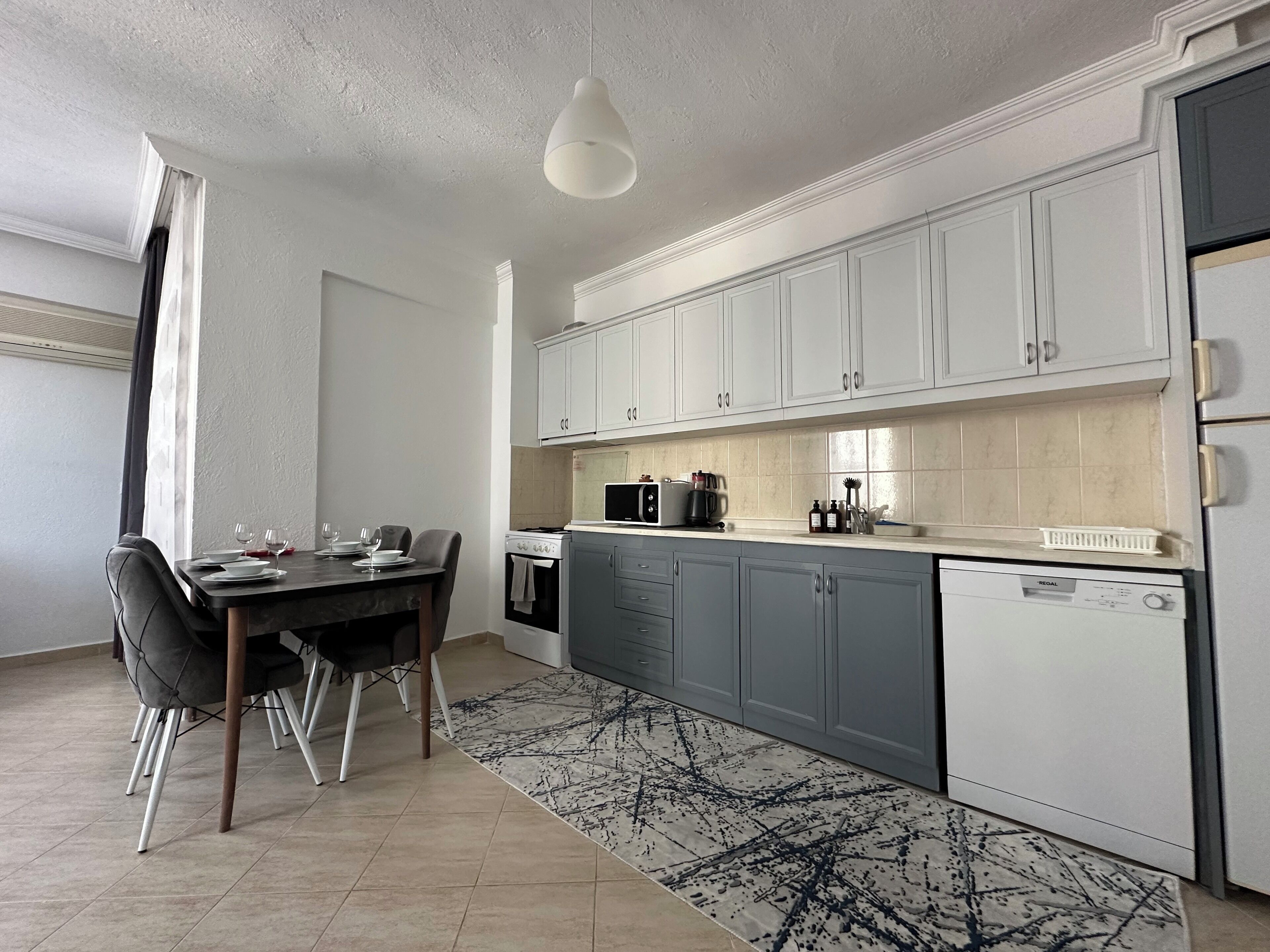 Una cocina moderna con armarios blancos, una mesa de comedor con sillas, microondas y lavavajillas.