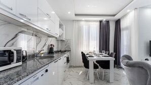 Une cuisine moderne avec des meubles blancs, un plan de travail en granit et un coin repas comprenant une table et des chaises blanches.
