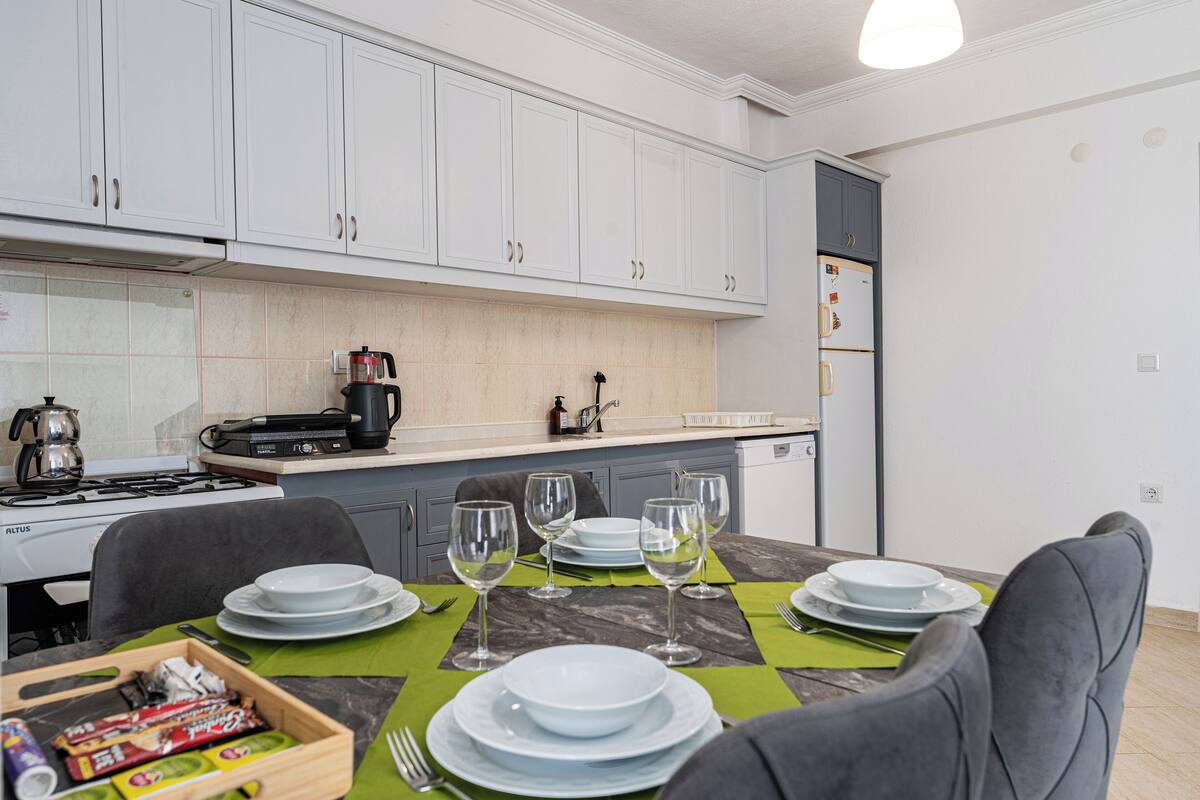 A modern kitchen with white cabinets, a gas stove, and a dining area set with plates, glasses, and cutlery.