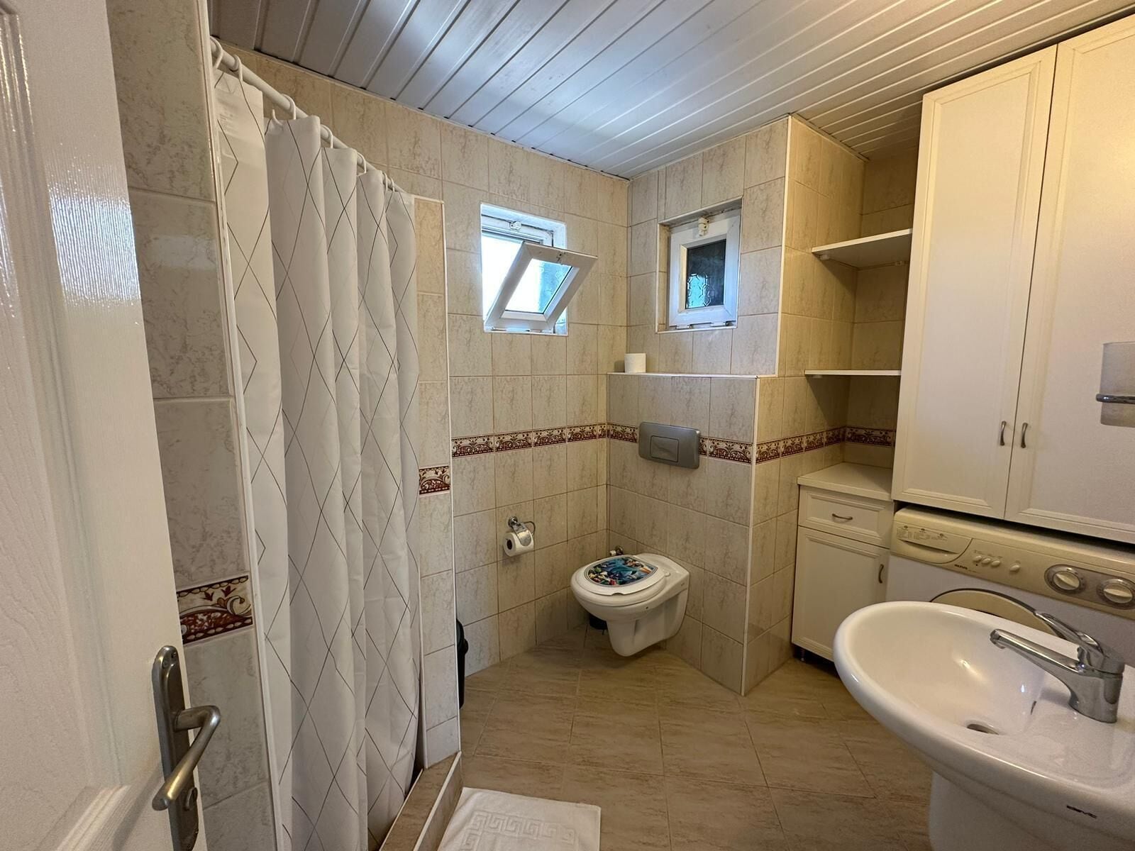 Ein kleines Badezimmer mit Dusche, Toilette, Waschbecken und einem kleinen Fenster.