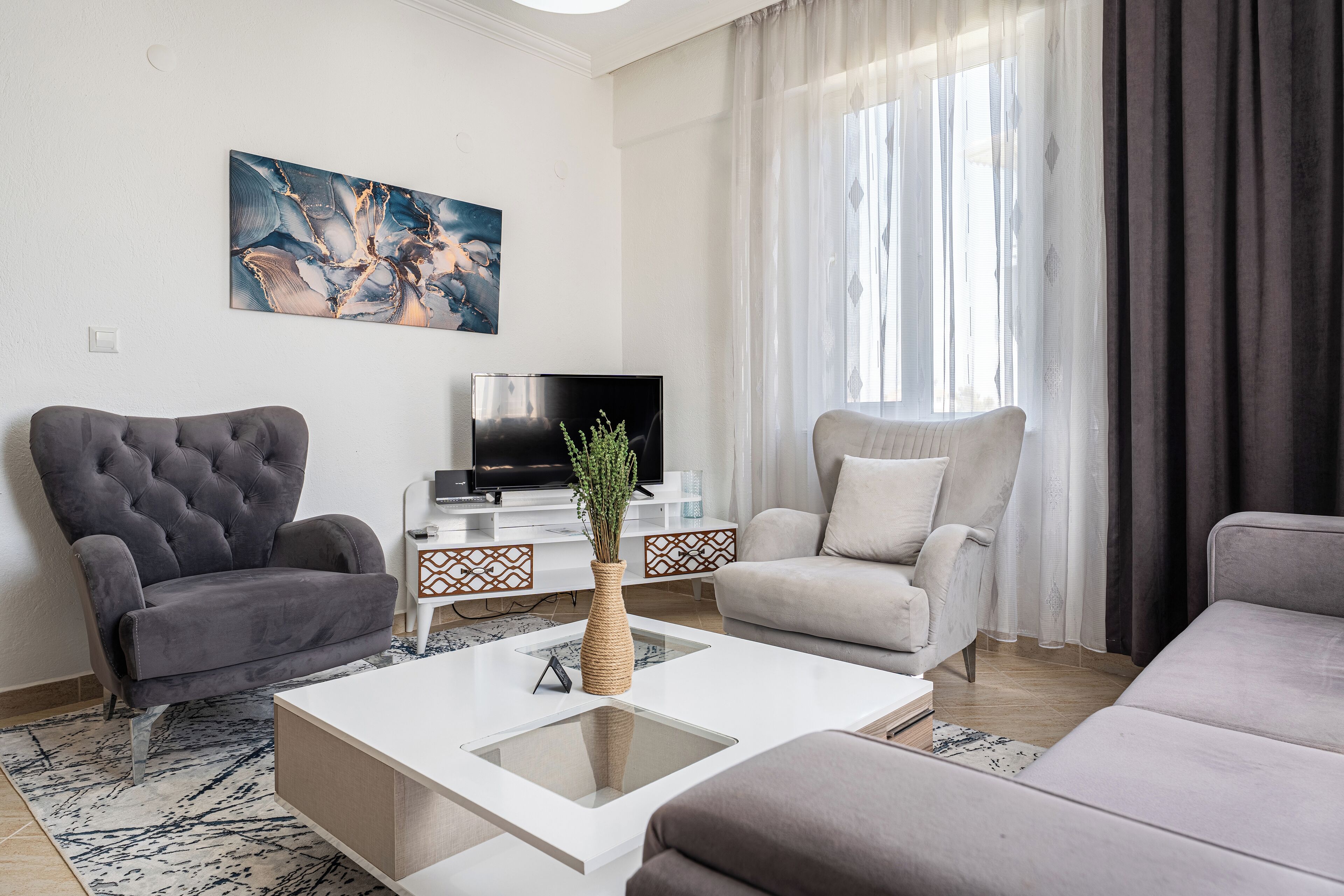 Ein modernes Wohnzimmer mit einem großen Flachbildfernseher, zwei Sofas, einem Couchtisch und einer dekorativen Vase.