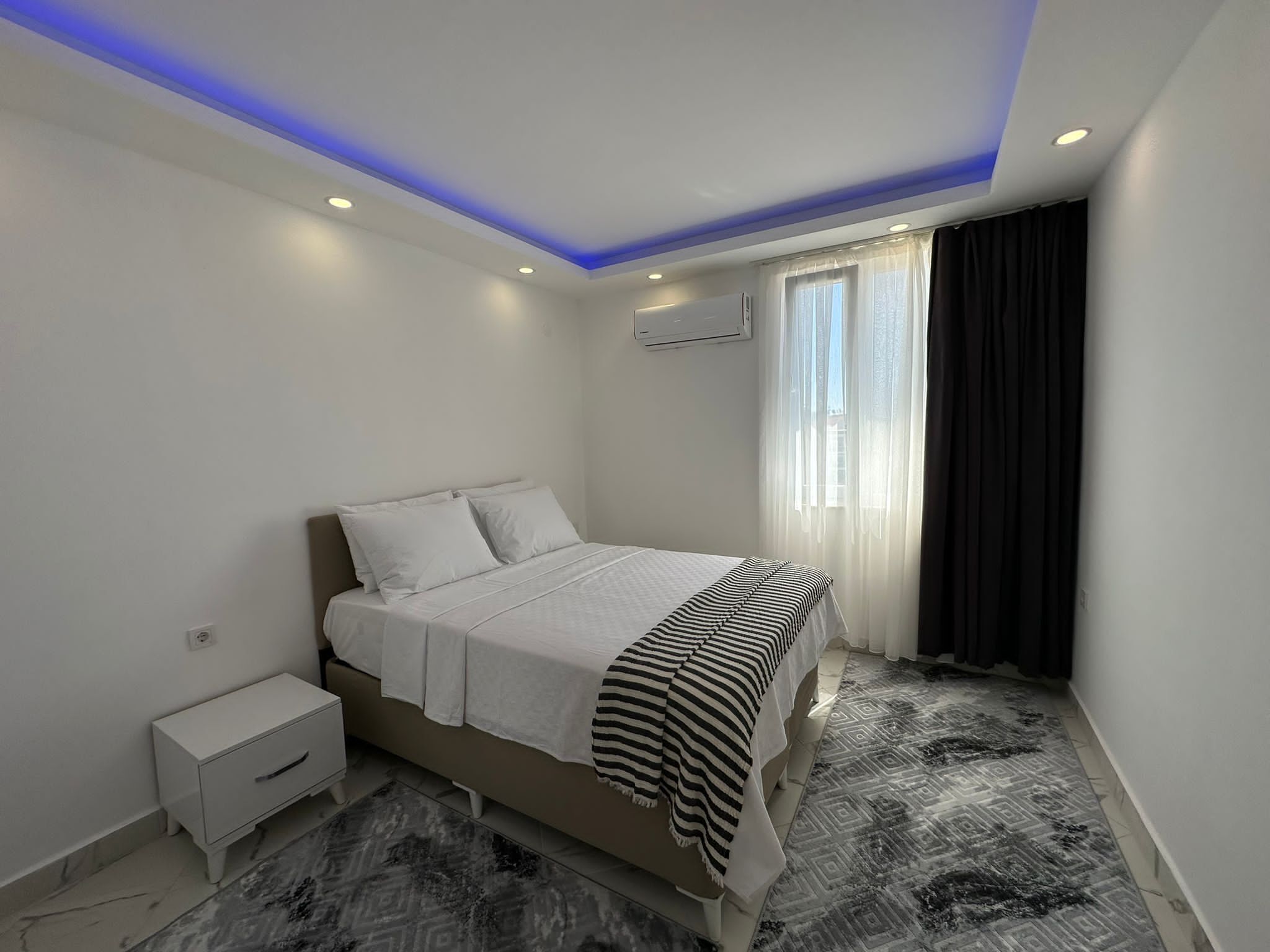 Un dormitorio moderno con una cama, una mesita de noche y una alfombra estampada.