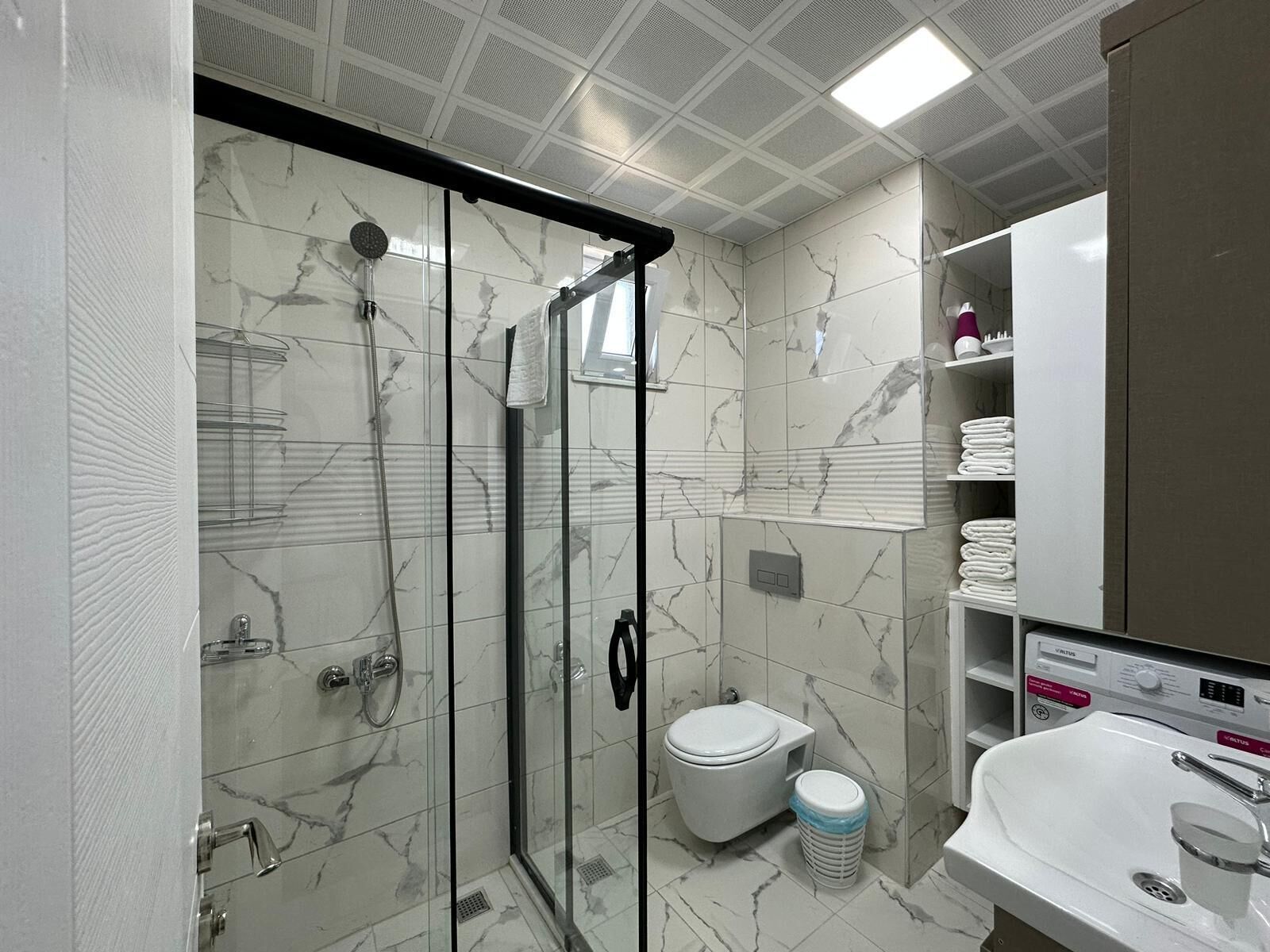 A modern bathroom with a glass-enclosed shower, a toilet, and a sink.