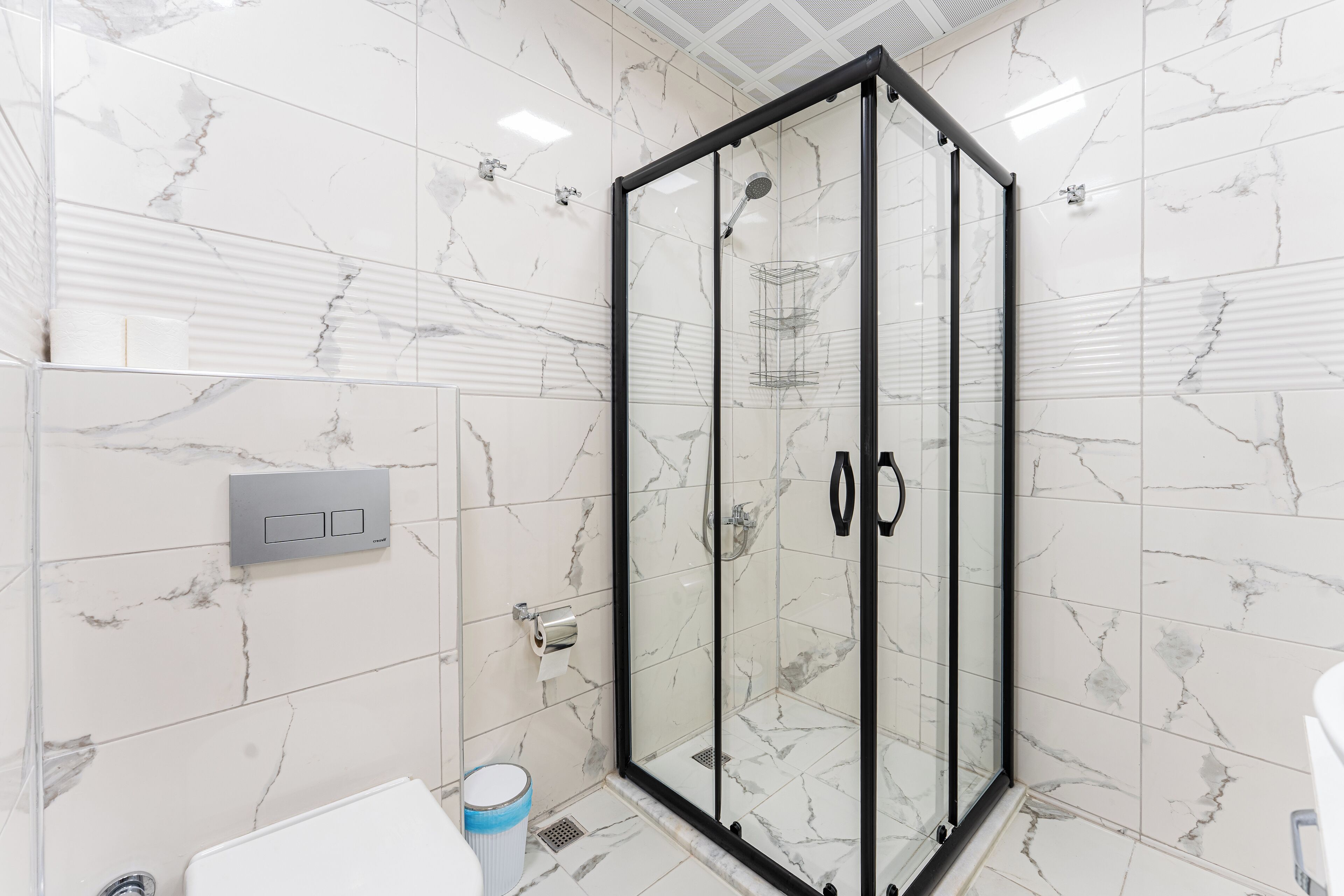 Un baño moderno con cabina de ducha de vidrio, azulejos de mármol, inodoro y lavamanos.