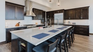 A modern kitchen with dark wood cabinets, stainless steel appliances, and a large island with bar stools. - Luxury Listing | A/C, Hot Tub, Close to Skiing, Incredible Mountain Views (Pagosa Springs)