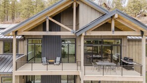 A modern two-story house with a balcony, large windows, and a grill area. - Luxury Listing | A/C, Hot Tub, Close to Skiing, Incredible Mountain Views (Pagosa Springs)
