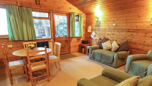 A cozy cabin interior with a wooden interior, a dining table with chairs, a sofa, and a small side table.
