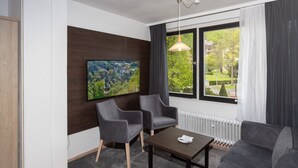 A modern living room with a large TV, two grey armchairs, a dark coffee table, and a grey sofa. - Villa Feise (Bad Harzburg)