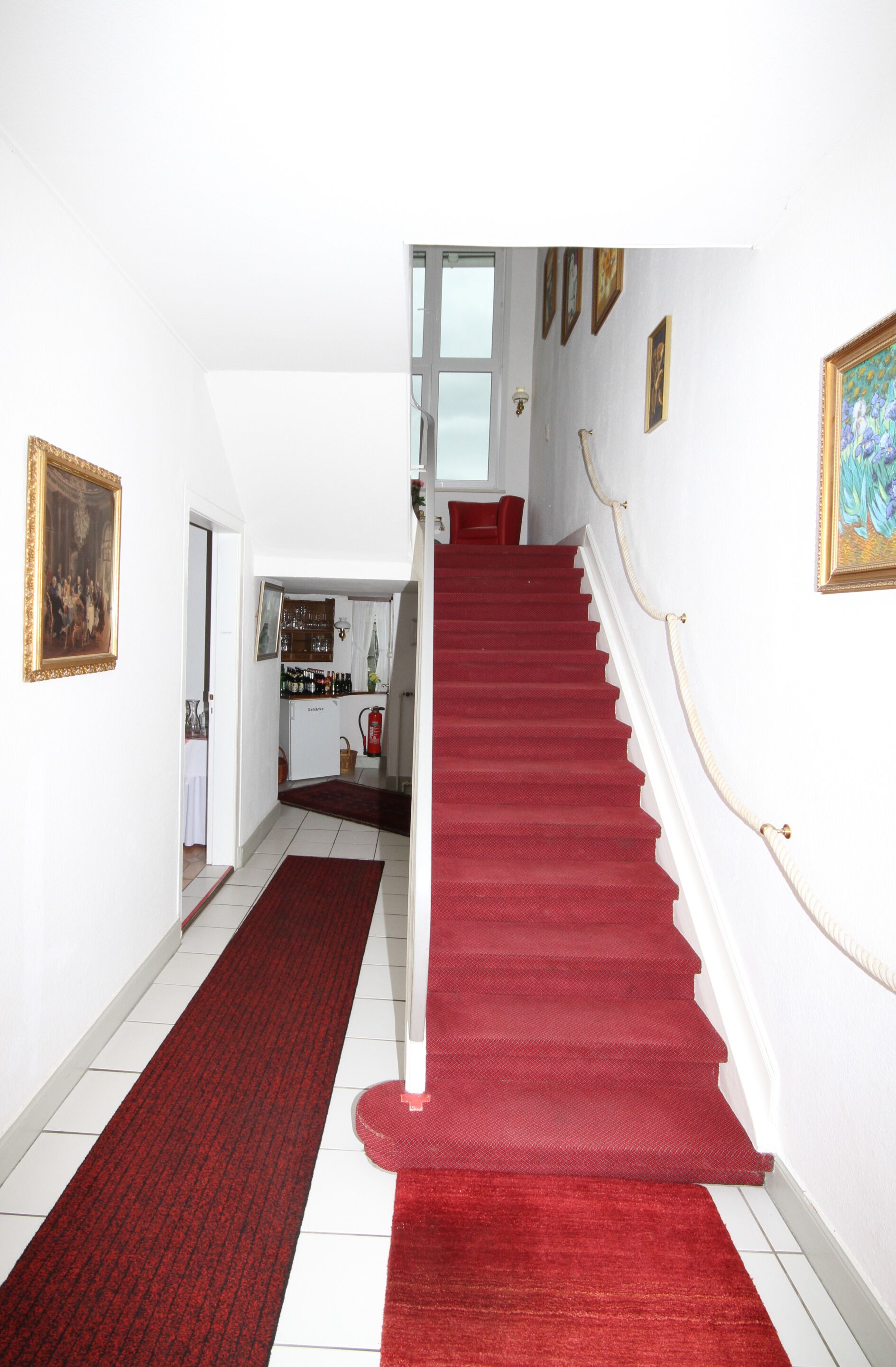 Eine Treppe mit rotem Teppich führt zu einer Empfangsebene mit einer Küche und einem Essbereich.