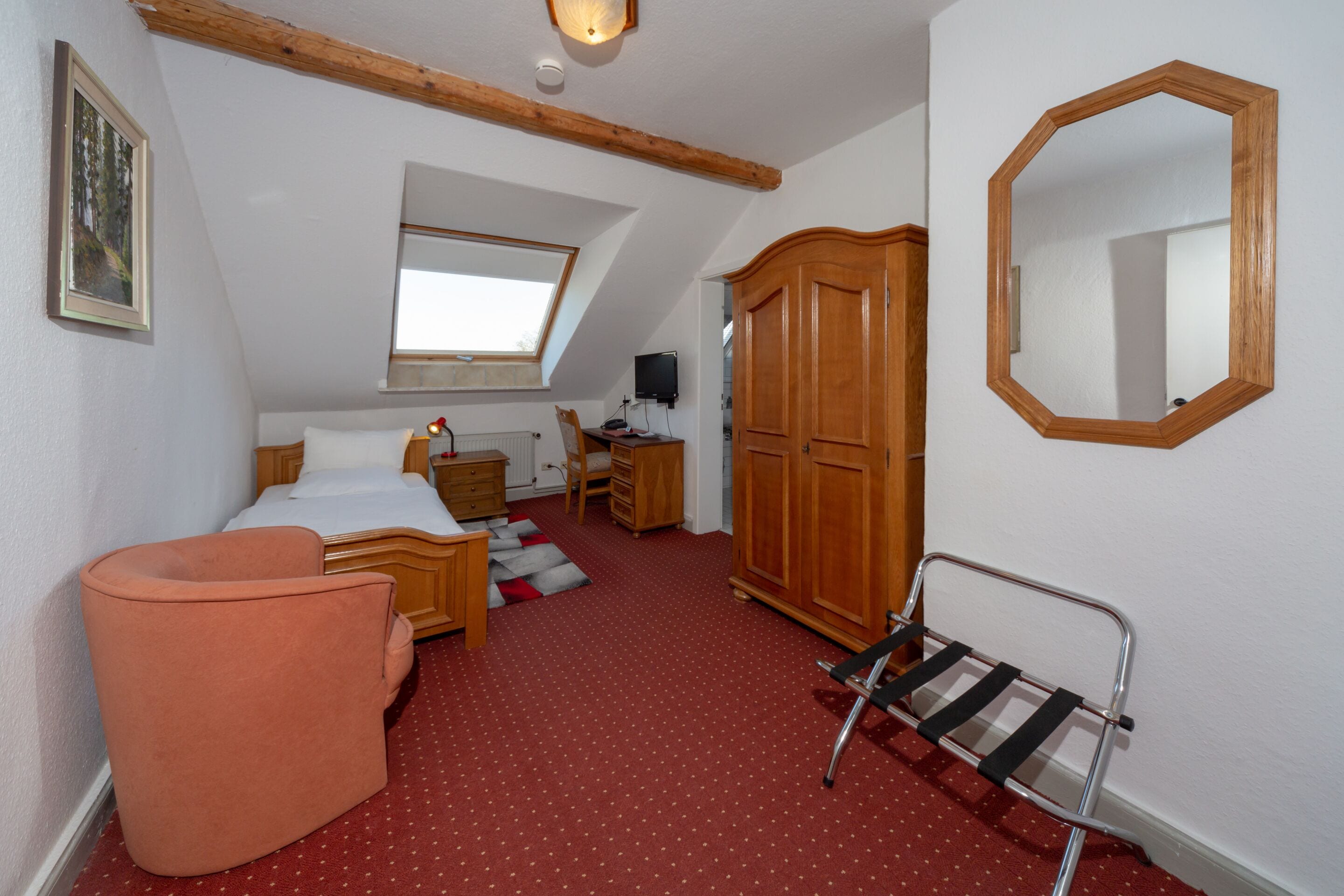Ein Schlafzimmer mit Bett, Sessel, Kleiderschrank, Spiegel, Schreibtisch und Fernseher.