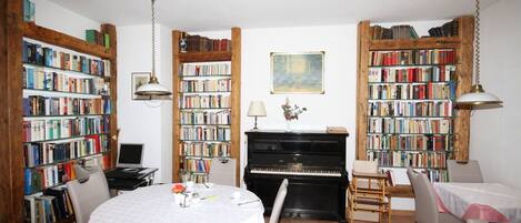 Una habitación con un piano, estanterías, una mesa de comedor y sillas.