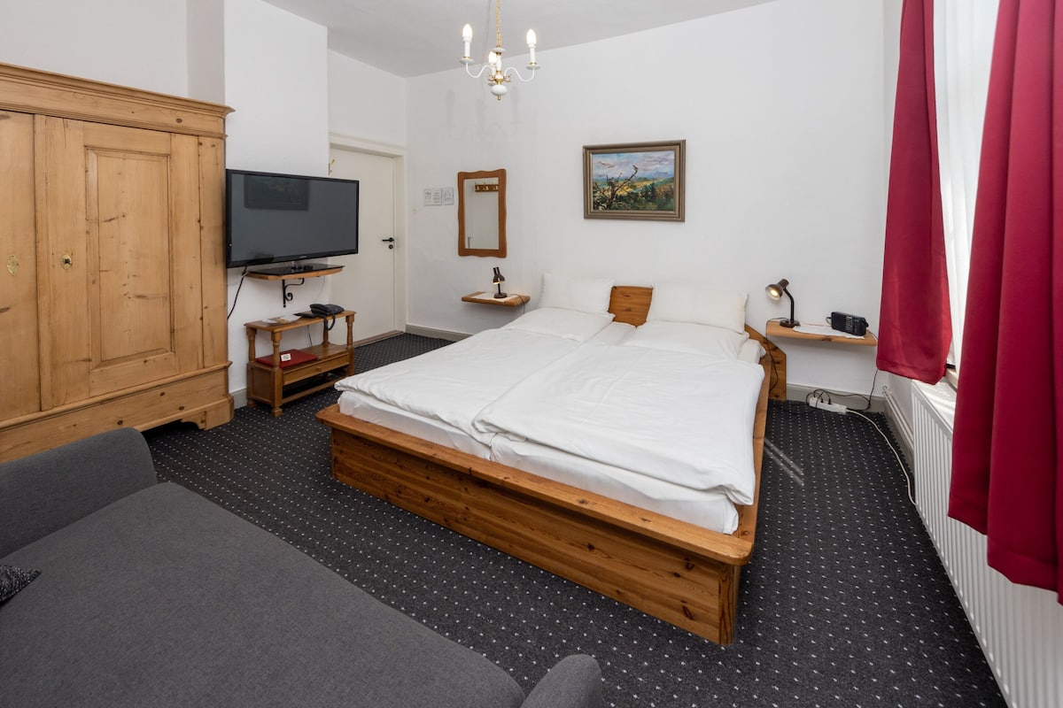 Un dormitorio con una cama de madera, televisor, espejo y cortina roja.