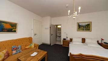 A hotel room with a wooden bed, a wooden table, a sofa with colorful cushions, a chandelier, and a painting on the wall.