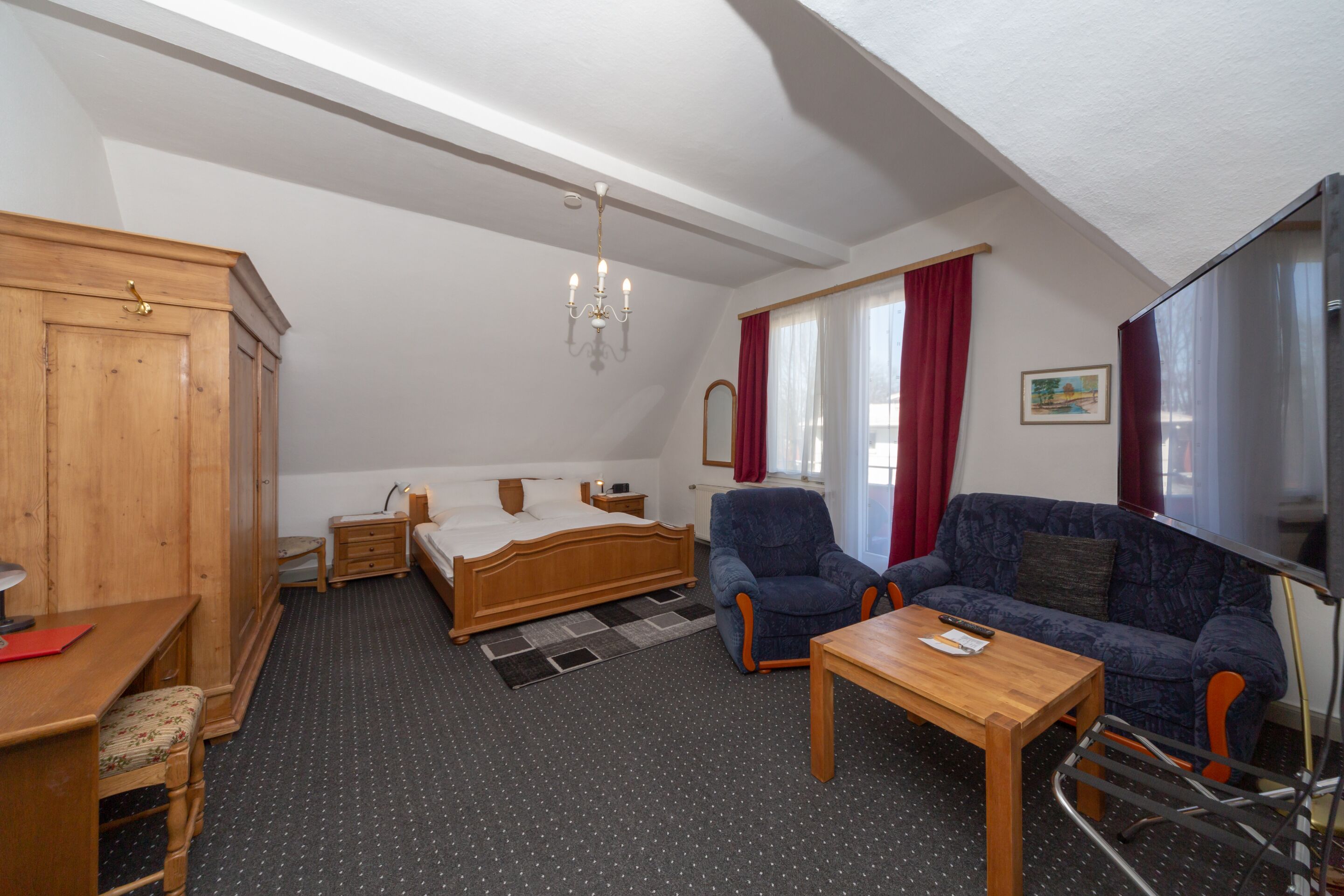 A bedroom with a bed, wooden wardrobe, desk, and chair.