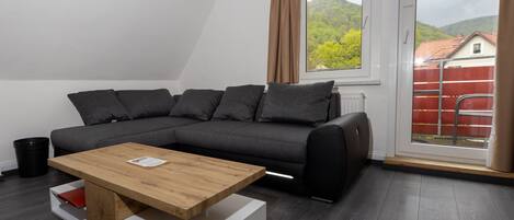 Una sala de estar moderna con un sofá gris oscuro, una mesa de centro de madera y vistas a un paisaje verde a través de un ventanal grande.