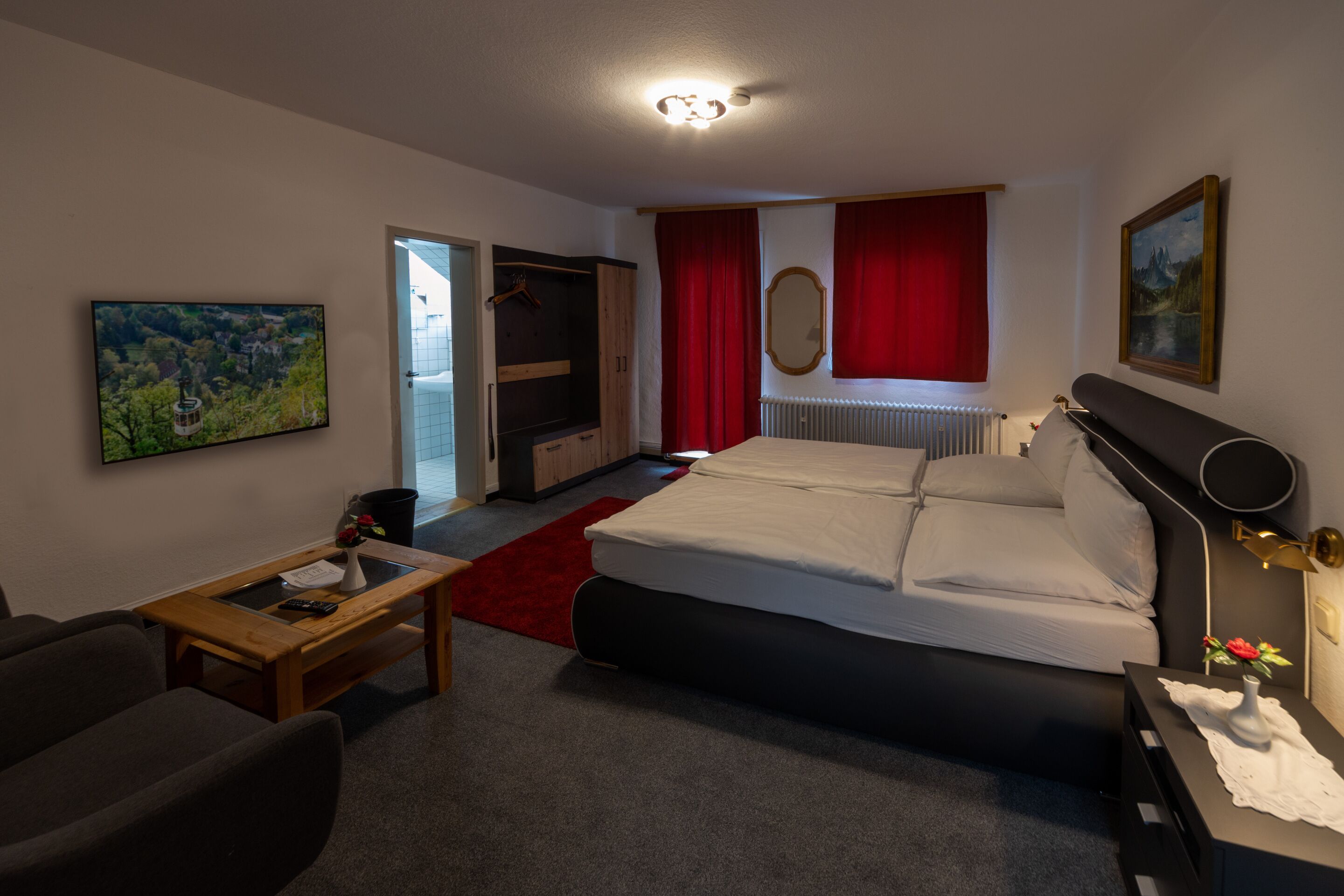 Un dormitorio con una cama, un escritorio, una silla, alfombra roja y un cuadro en la pared.