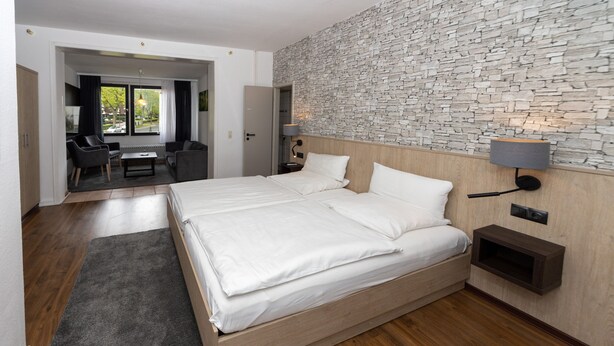 A modern hotel room with a large bed, a seating area with a table, and a stone wall. - Villa Feise (Bad Harzburg)