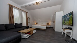 A modern, well-lit room with a dark grey sofa, a wooden coffee table, a white bed with a wooden headboard, and a small white table with a lamp. - Villa Feise (Bad Harzburg)