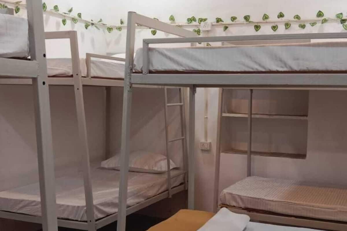 Un dormitorio con literas metálicas, suelo de madera y un equipo de aire acondicionado en la pared.