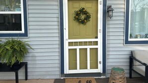 A house with a front door, a wreath, a doormat, a potted plant, and a bench.