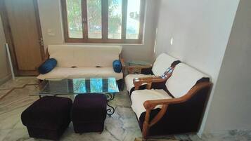 A living room with a sofa, armchairs, a glass coffee table, and a patterned rug.