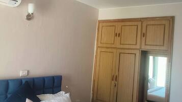 Une chambre avec un grand lit, un ventilateur de plafond, une armoire en bois et une petite fenêtre.
