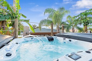 A hot tub with a wooden deck and a view of palm trees and a building in the background.