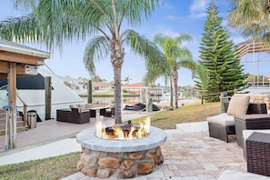 An outdoor patio with a stone fire pit, wicker furniture, and palm trees.