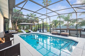 A pool area with a glass enclosure, lounge chairs, and a view of palm trees. - Canal Front Oasis With Pool in Palm Coast (Palm Coast)
