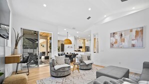 A modern living room with grey sofas, a patterned rug, and a dining area in the background. - Luxury Retreat With Pool in Palm Coast (Palm Coast)