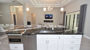 A modern kitchen with a large island, stainless steel appliances, and a flat-screen TV. - The Beach Pool Game Retreat (Palm Coast)