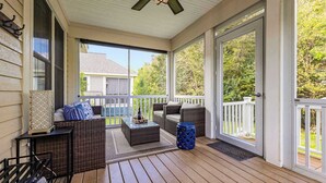 Une véranda couverte, meublée de meubles en osier, dotée d’un ventilateur de plafond et offrant une vue sur le jardin arrière.
